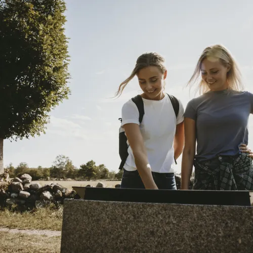 två tjejer står och läser på en informationstavla vid Mittlandsleden på Öland. 