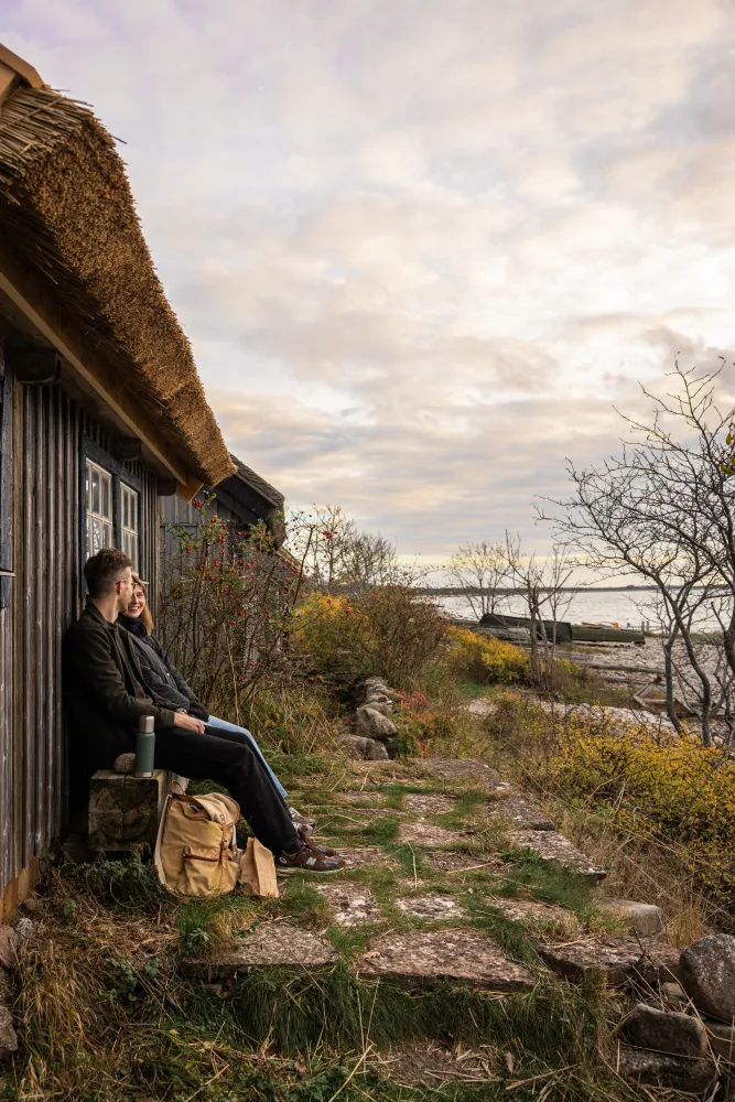 Två personer på sitter på en bänk lutade mot ett hus