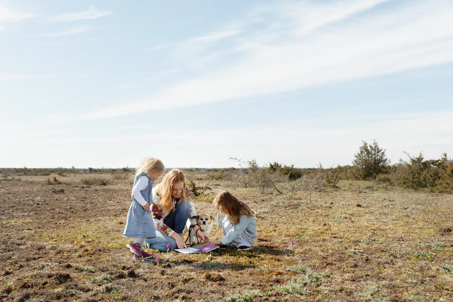 En kvinna och två barn sitter på marken med en hund och tittar på orkidéer tillsammans.