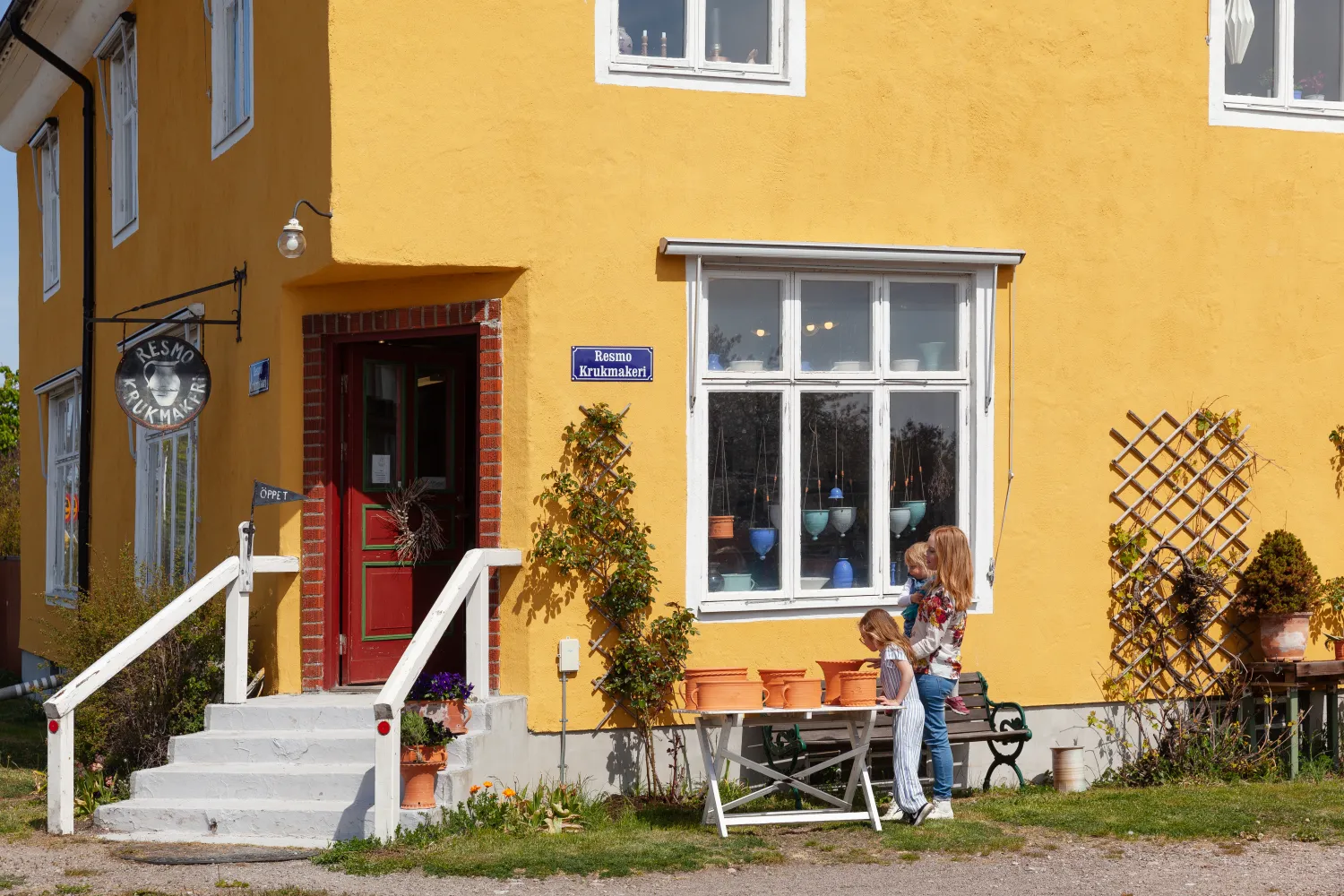 Ett gult hus med en entré till Resmo krukmakeri där en kvinna och ett barn står utanför.