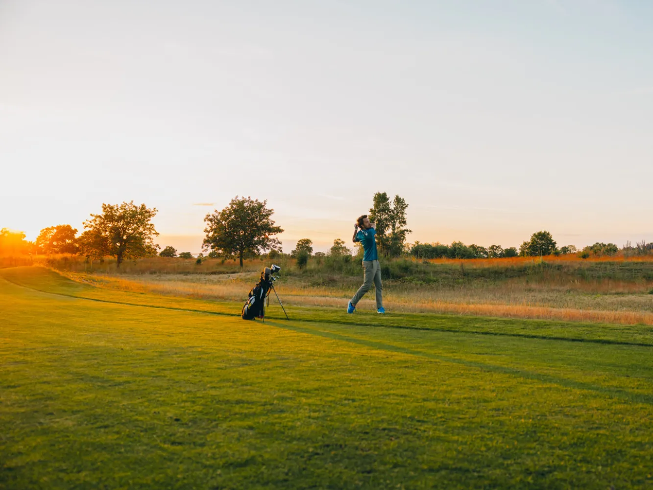 En golfare som svingar sin klubba på en höstig golfbana med solnedgång i bakgrunden