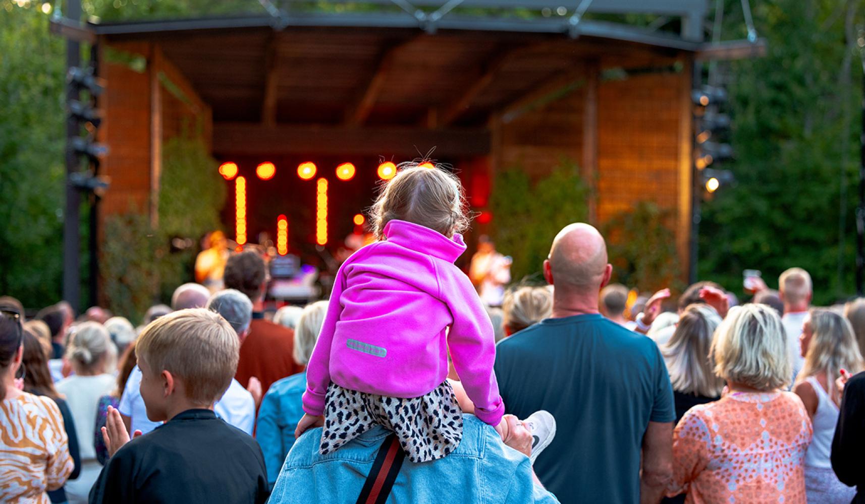 Little girl sits on dad's shoulders and watches concert