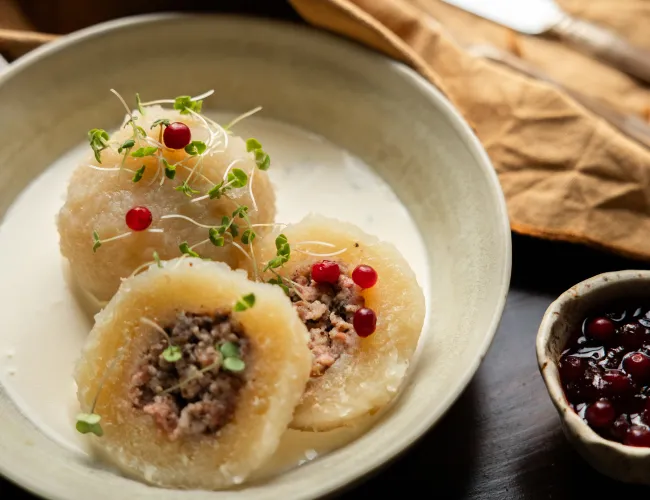 Kroppkakor på en tallrik med råröda lingon och grädde