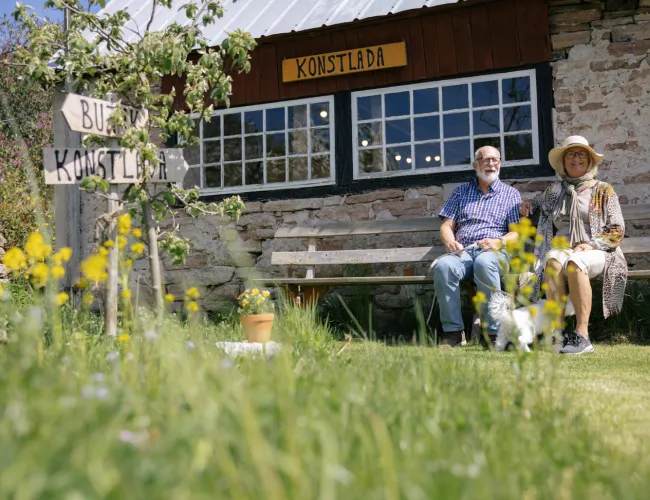 Ett par sitter på en bänk utanför en konstlada på Öland