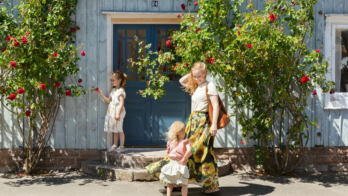 En kvinna och två barn står utanför ett hus med rosor.
