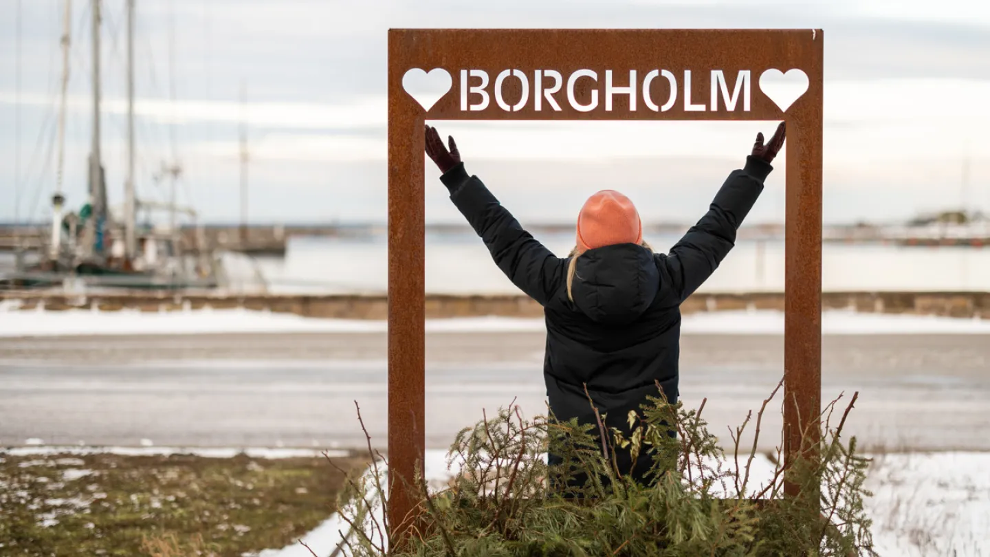 En glad tjej står med armarna uppåt vid Borgholms skylt i gästhamnen.