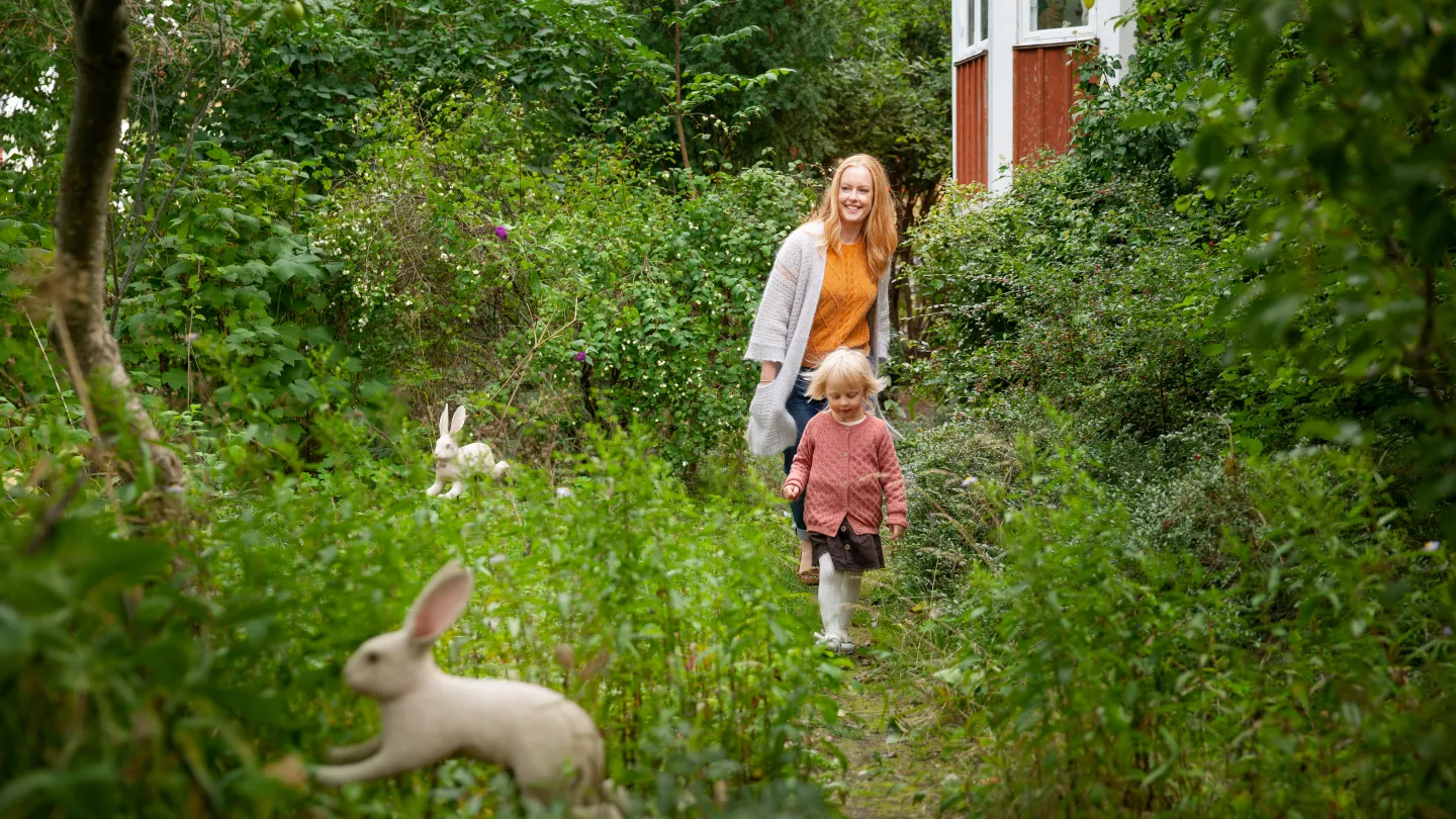 En kvinna och ett barn går på en stig i grönskande natur.
