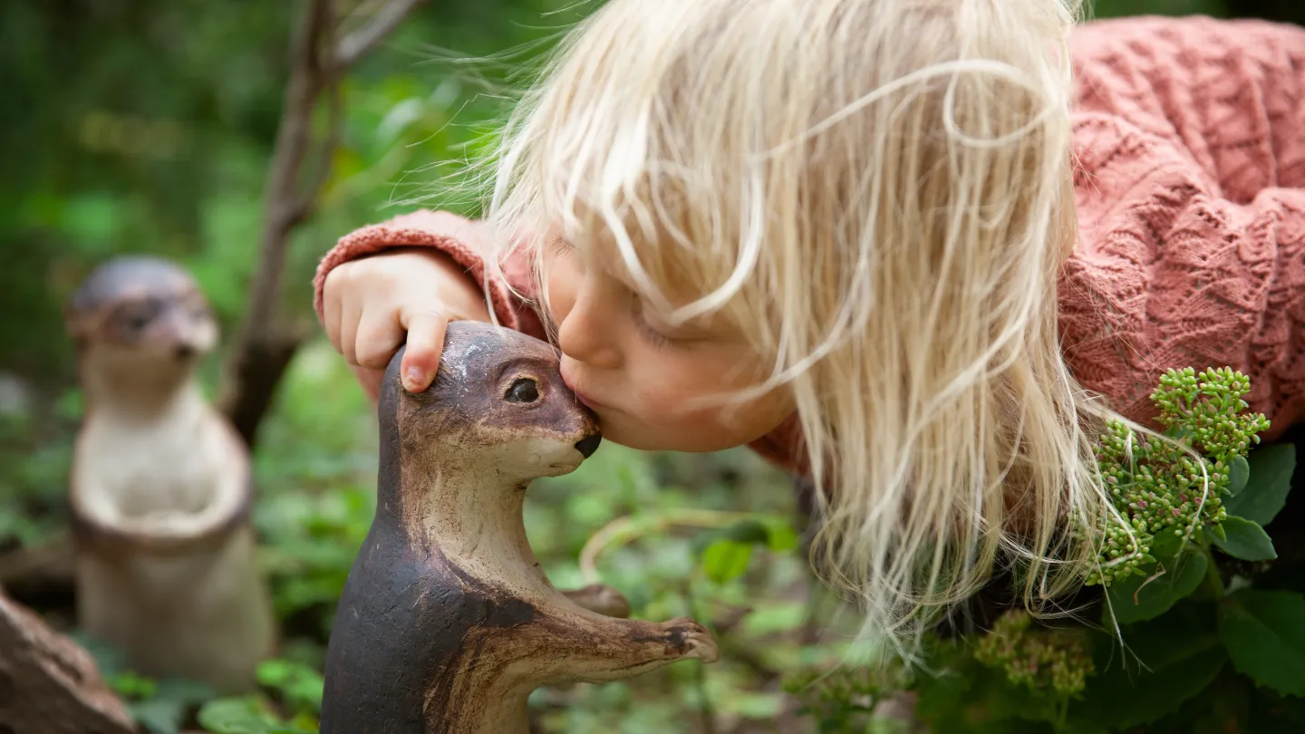 Ett barn pussar en liten figur i naturen.