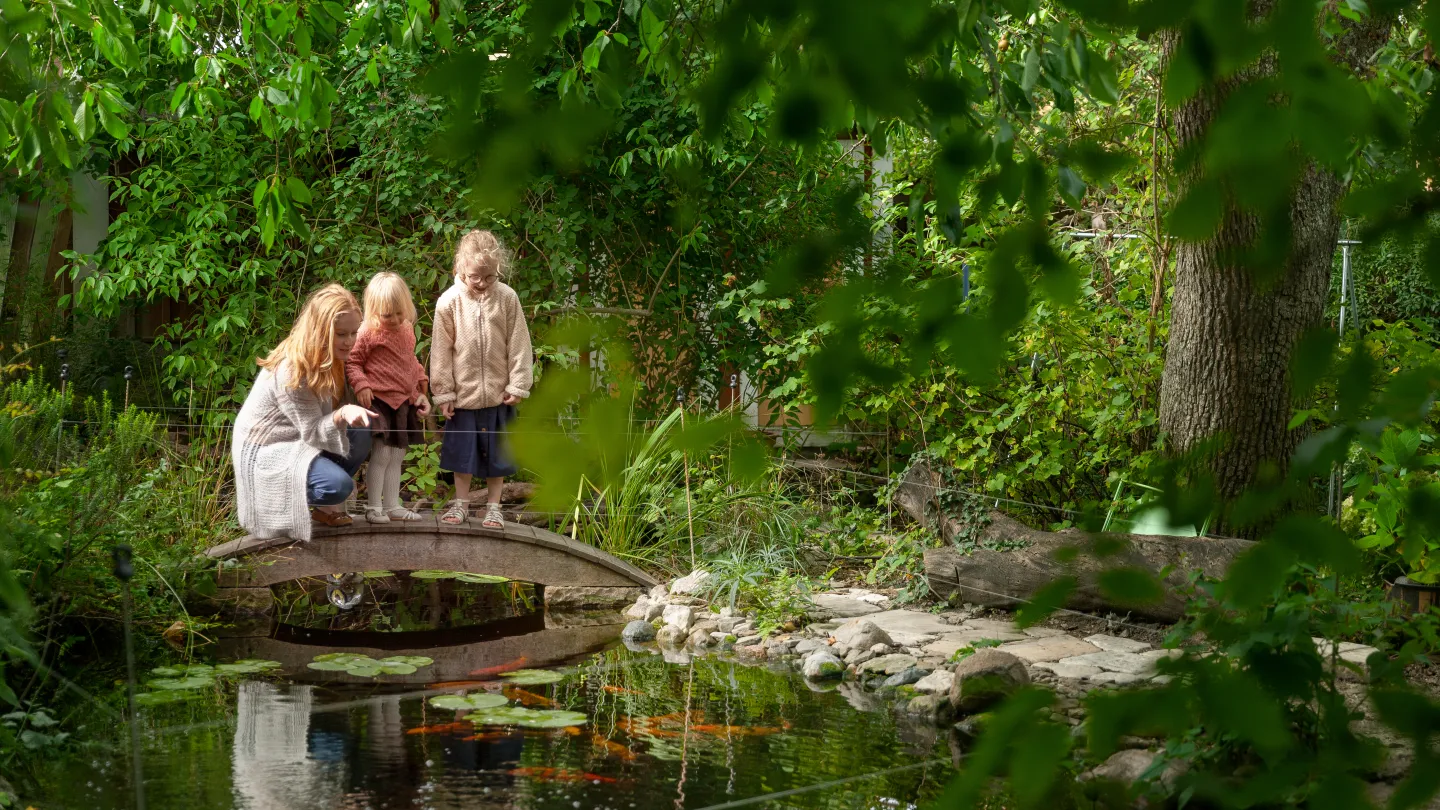 En kvinna och två barn står på en liten bro vid en damm.