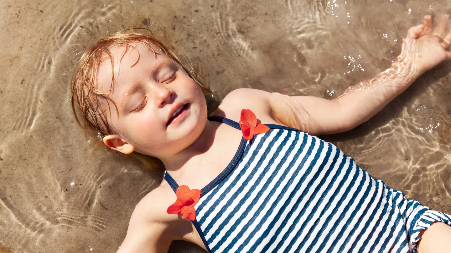 Ett barn ligger i grunt vatten på stranden.