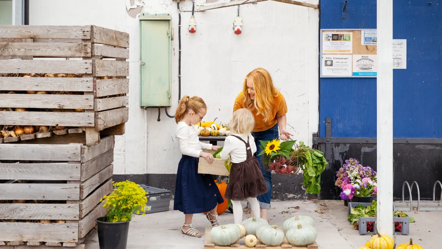 En kvinna och två barn handlar frukt och grönsaker.