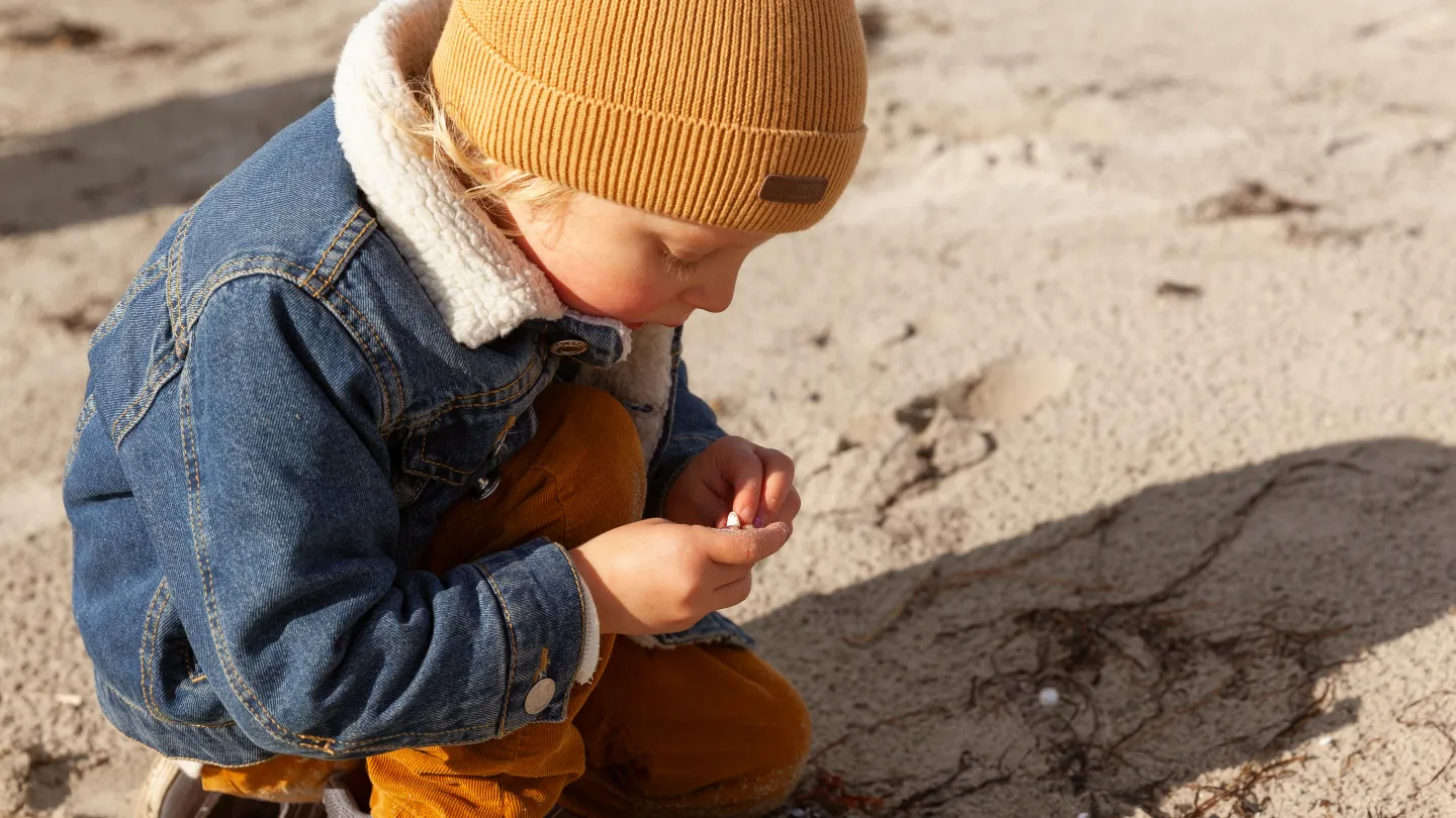 Et barn sitter och kollar på en snäcka på en strand