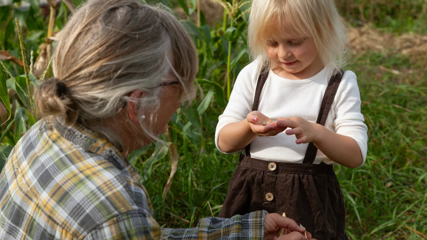 Ett barn står och kollar ner i sin hand där bönor ligger