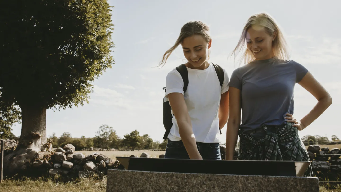 Deux jeunes filles sont debout et lisent un panneau d'information sur le sentier Mittlandsleden, sur l'île d'Öland. 