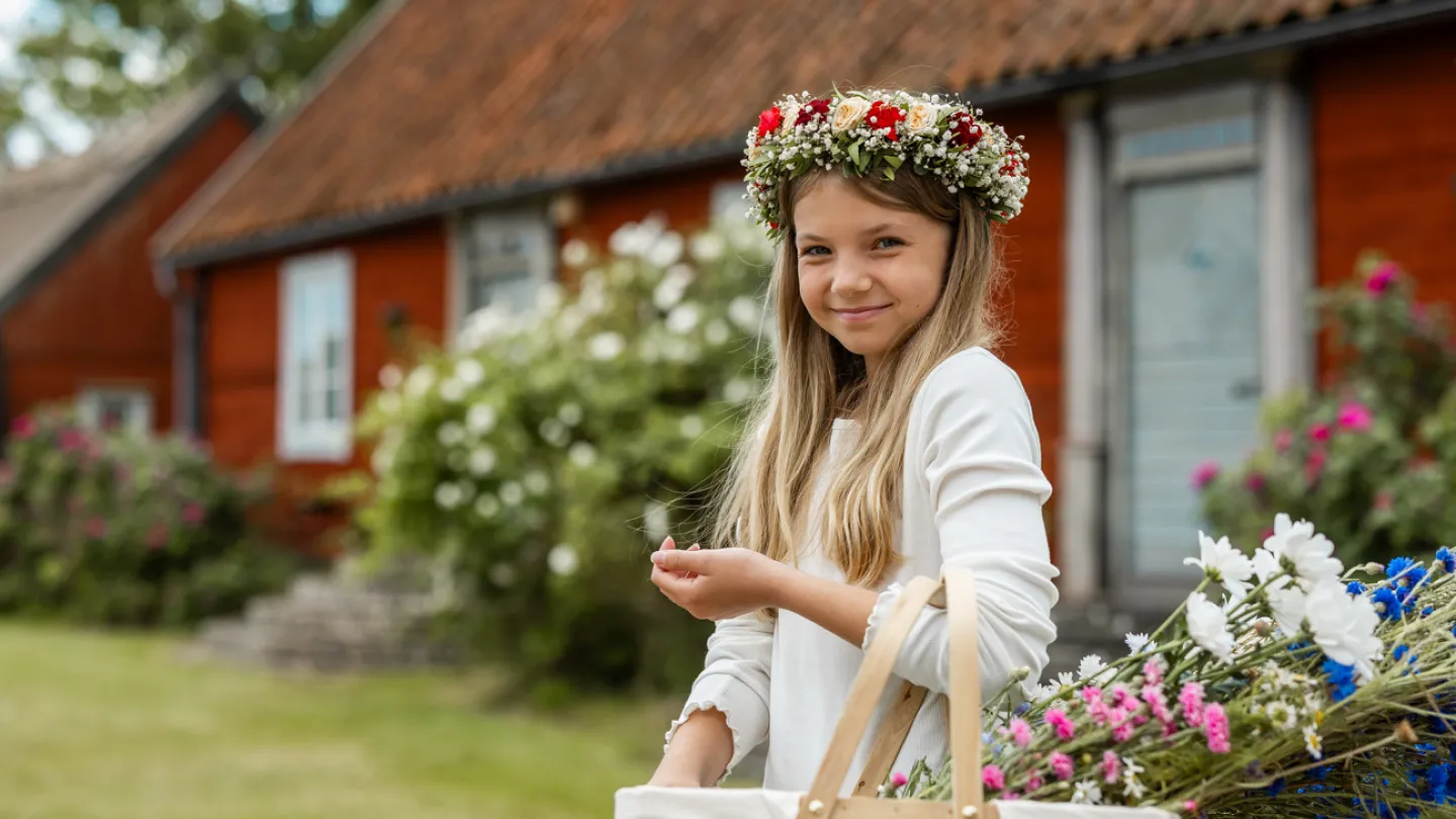 En liten tjej med en vacker midsommarkrans håller en korg med midsommarblommor