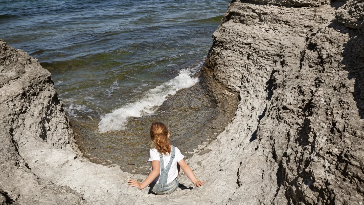 Ett barn sitter vid klipporna och tittar ut över havet.