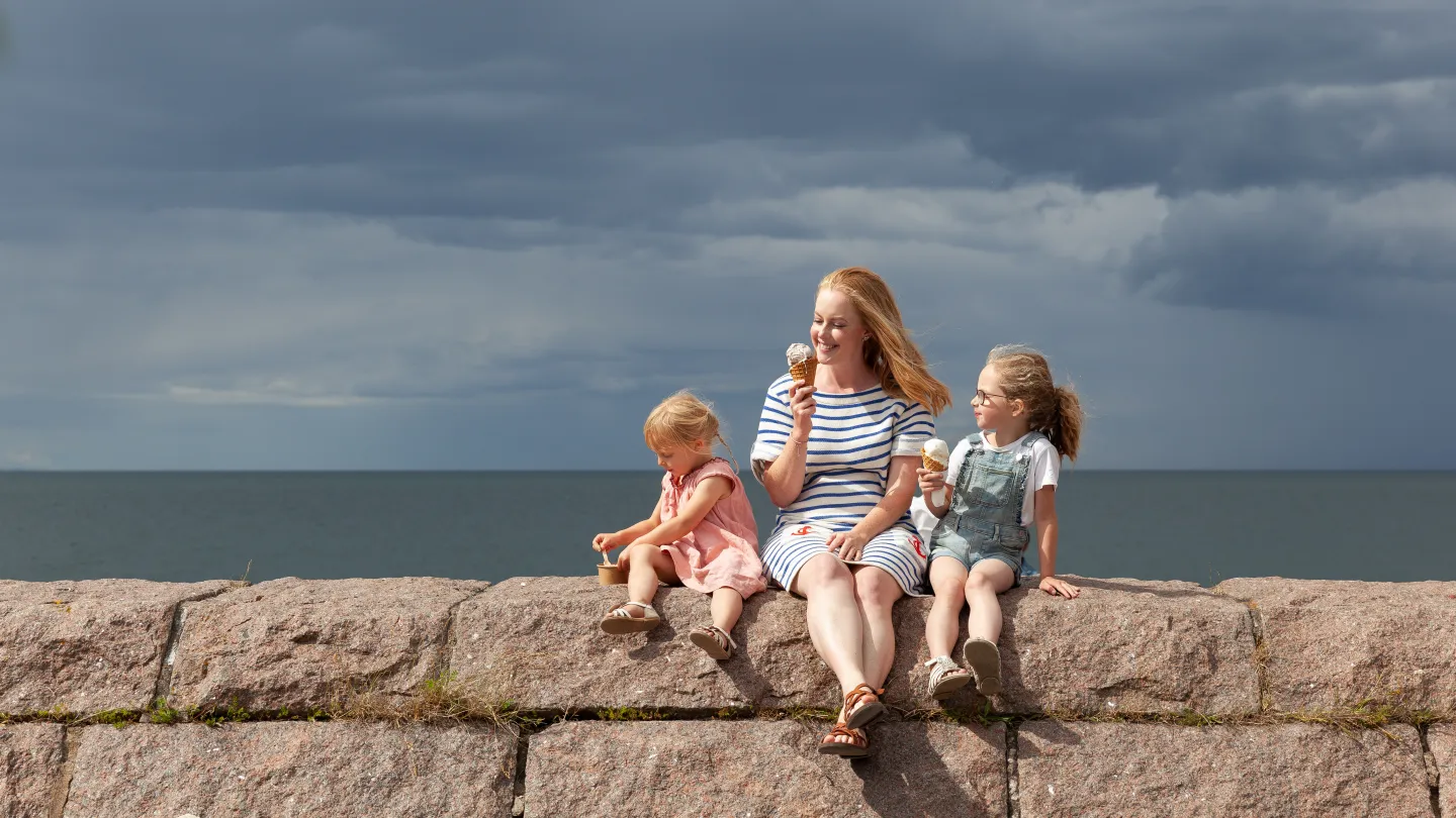 En kvinna och två barn sitter och äter glass på en stenmur