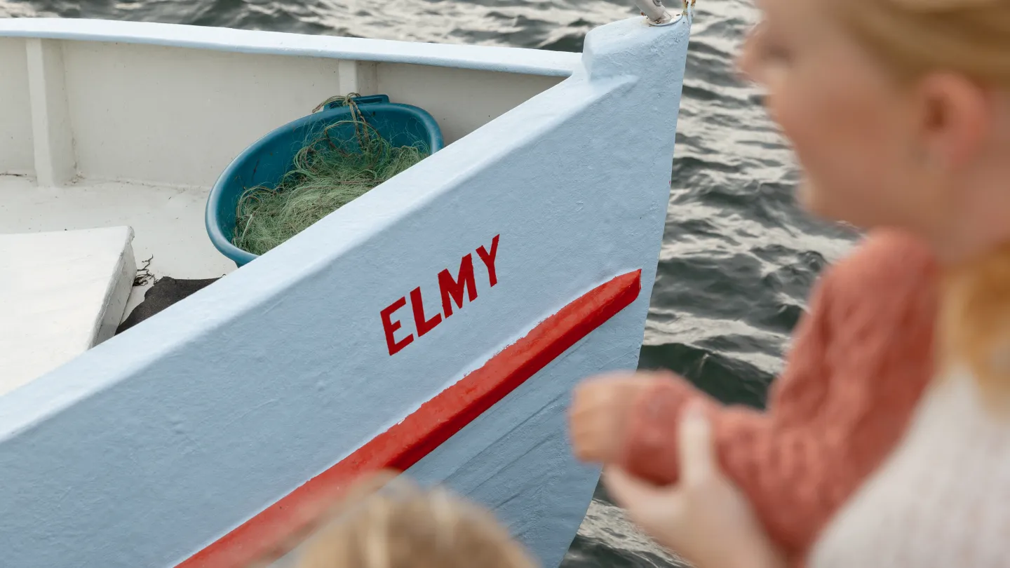 En båt ligger vid vattnet medan personer står bredvid.