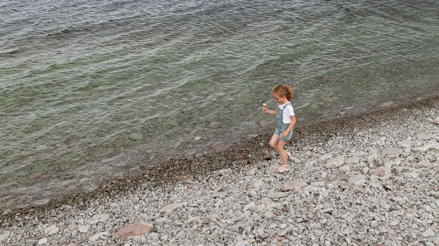 Barn som går på stenstranden längs vattnet