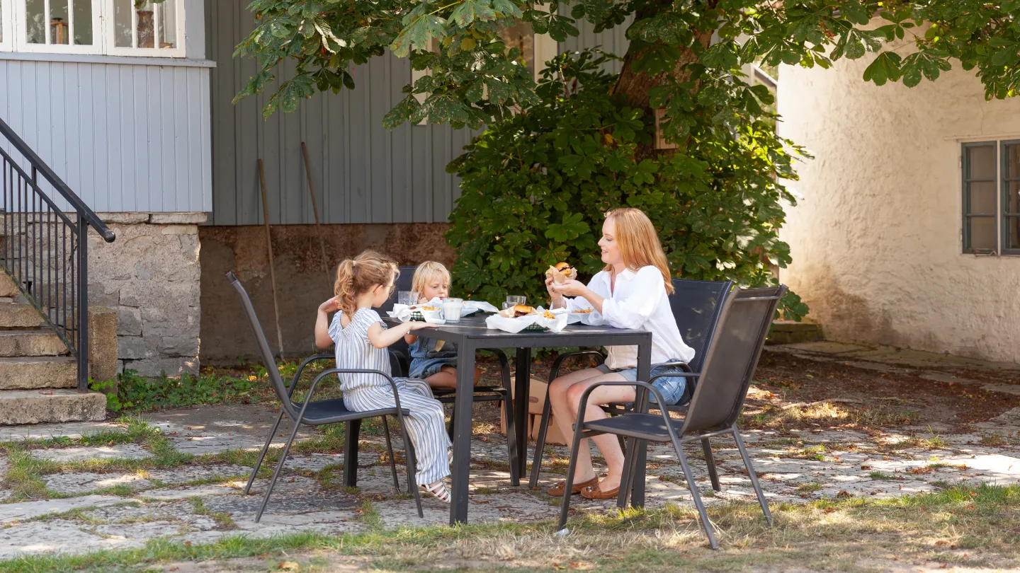 En kvinna och två barn sitter vid ett bord utomhus och äter.