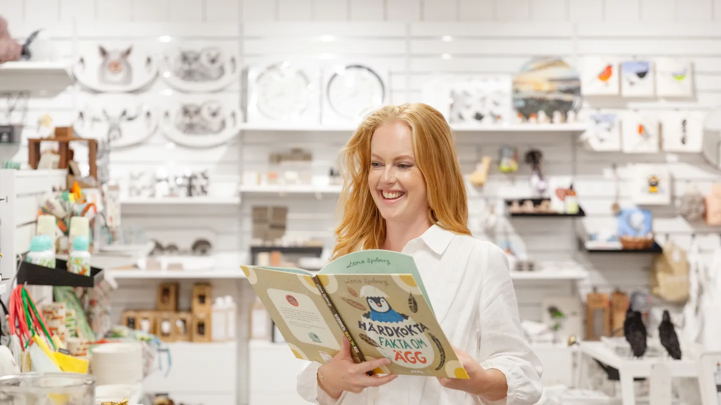 En kvinna står i en butik och läser en bok.