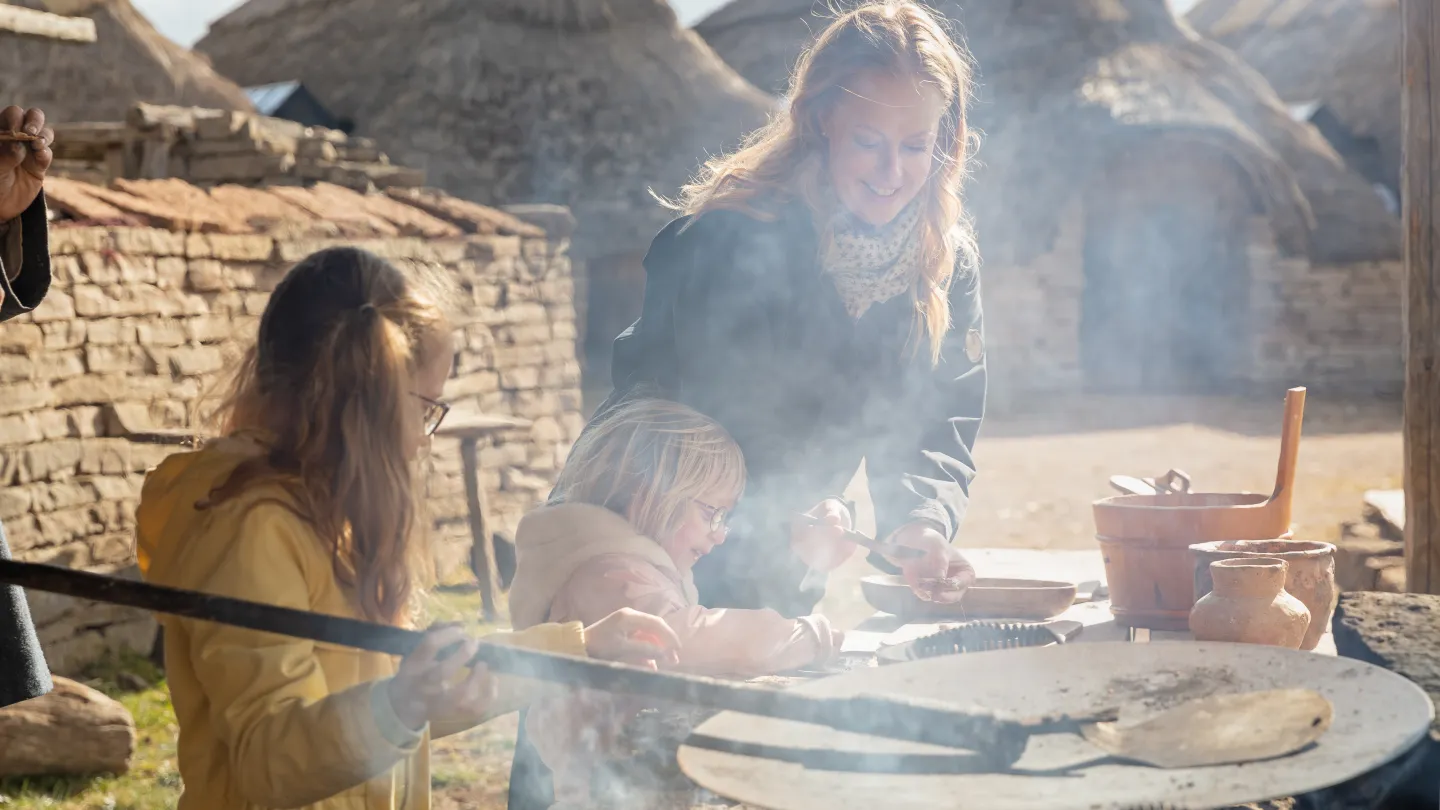 Barn och vuxen lagar mat över öppen eld. 