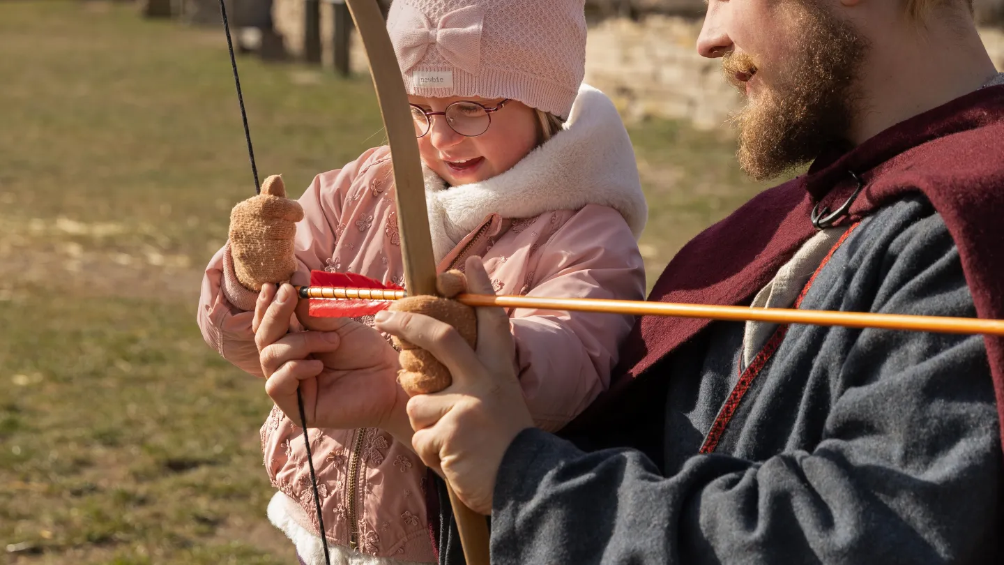 Barn provar bågskytte med hjälp av vuxen.