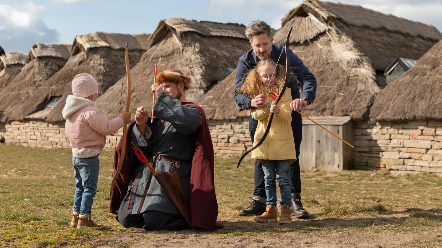 Barn testar pilbåge med hjälp av vuxna