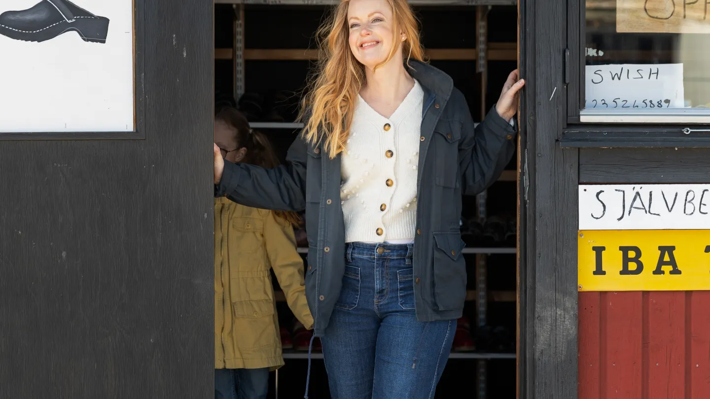 Kvinna står vid öppningen av en dörr och ler