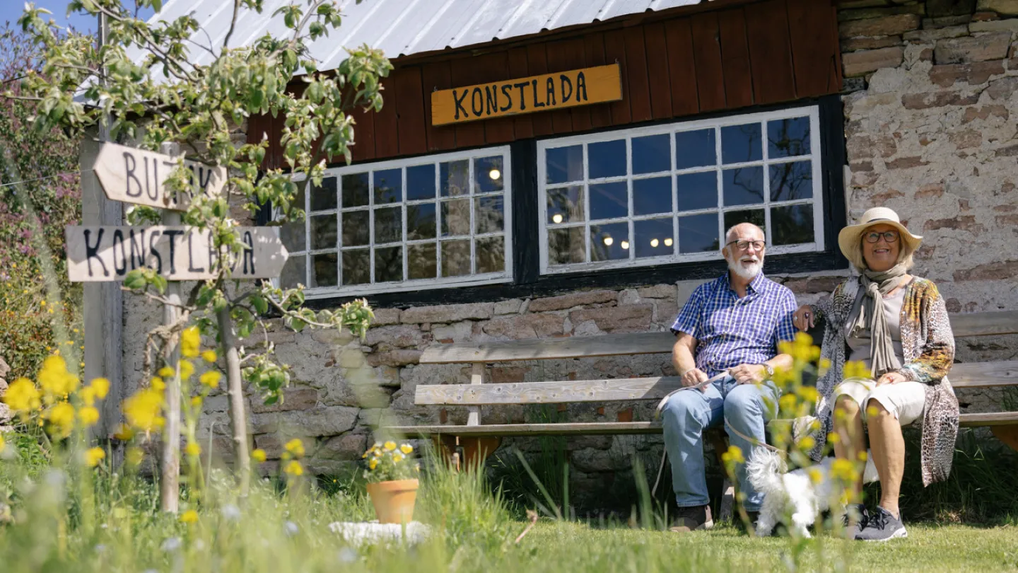 Ett par sitter på en bänk utanför en konstlada på Öland