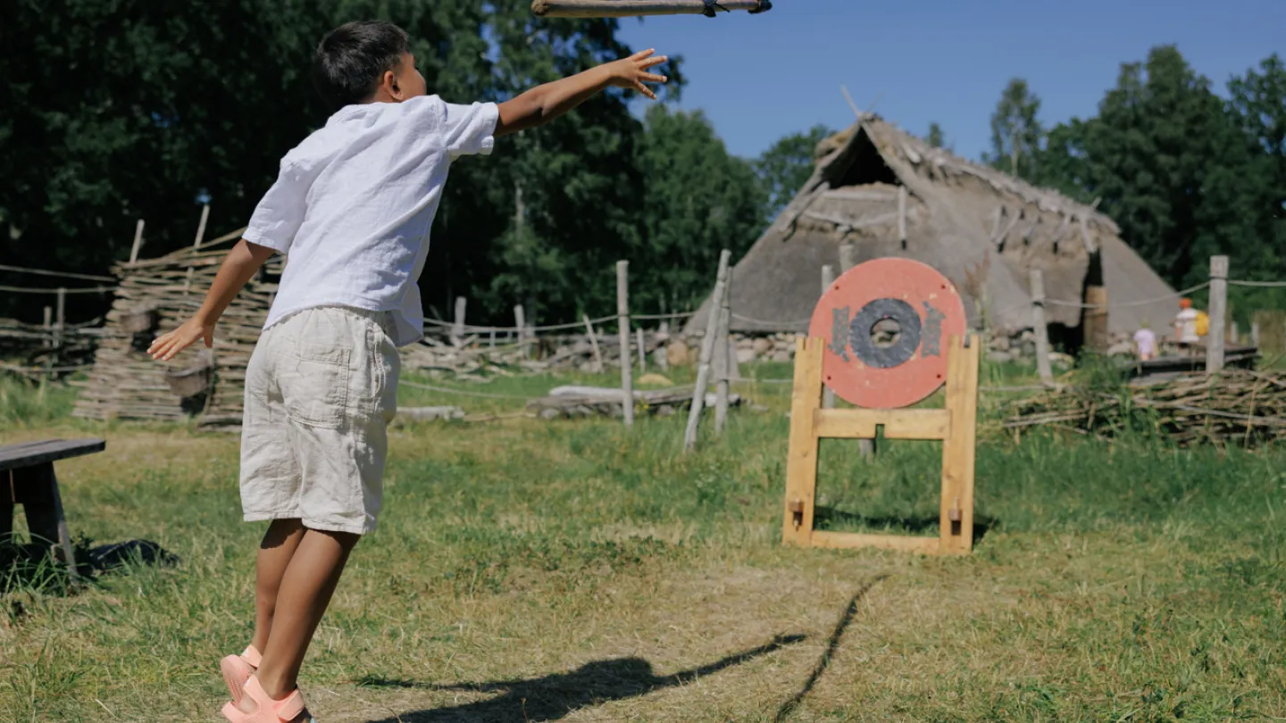 En liten kille kastar ett spjut vid Skäftekärrs järnåldersby på Öland. 