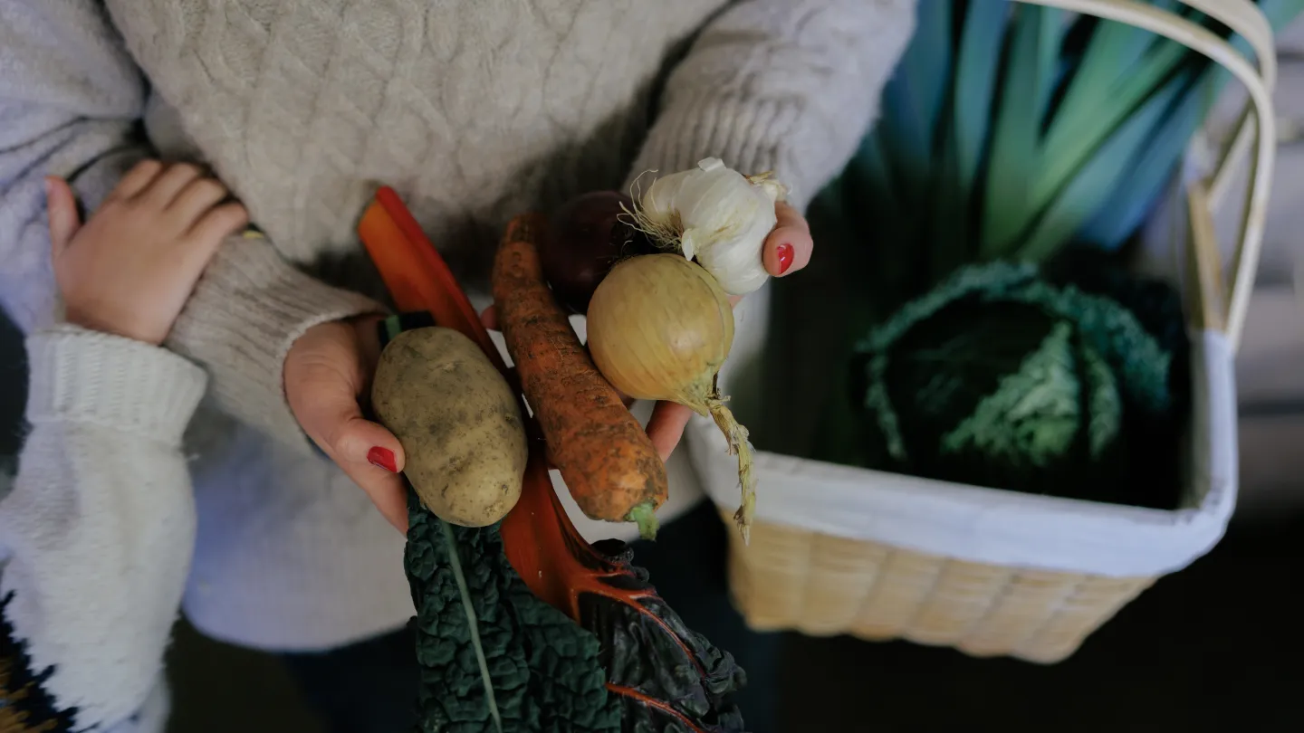 Person håller i rotfrukter och en korg i en gårdsbutik på Öland.